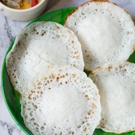 overhead shot of kerala appams on a green plate with vegetable stew in white bowl placed on top