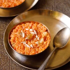 gajar ka halwa in a bronze bowl on a bronze plate with a bronze spoon by side