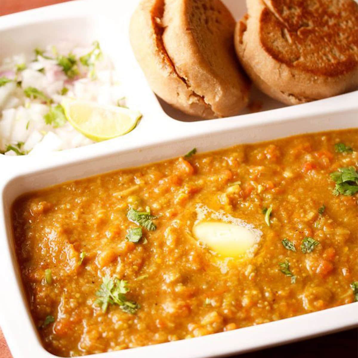 instant pot pav bhaji garnished with coriander leaves and served in a white tray with toasted pavs and chopped onions and lemons. 