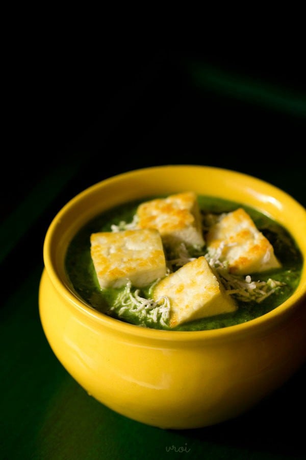palak paneer filled in a yellow ceramic bowl topped with lightly golden paneer cubes and grated paneer