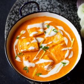 paneer butter masala served in a blue rimmed white pan, garnished with cream and cilantro