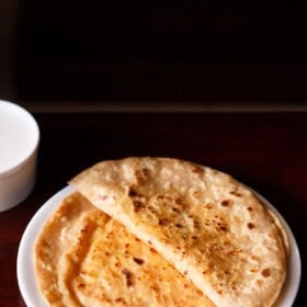folded paneer paratha on top of a paneer paratha on a white plate on a dark brown table