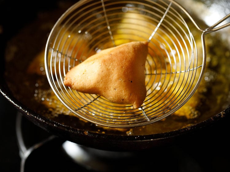 crispy fried samosa in a skimmer spoon 